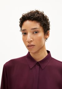 Burgundy shirt with a collared design, soft fabric, and button front. Features a smooth texture and tailored fit. Simple and elegant.