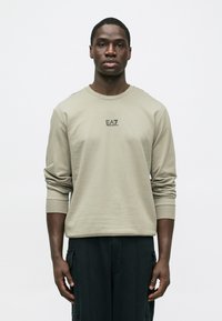 Ανοιχτό γκρι μακρυμάνικο πουκάμισο από απαλό βαμβακερό μείγμα, με στρογγυλή λαιμόκοψη και τυπωμένο λογότυπο EA7 στο στήθος. Ομαλή υφή και εφαρμοστό σχέδιο.