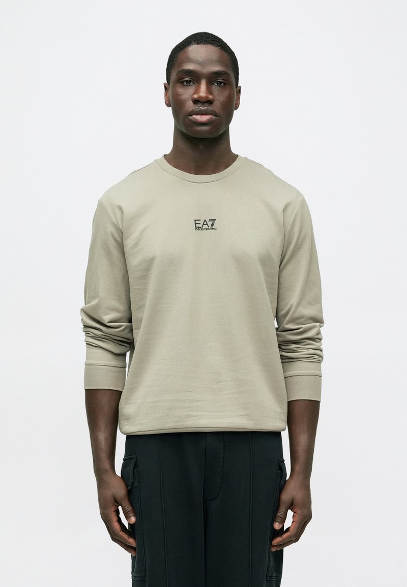 Ανοιχτό γκρι μακρυμάνικο πουκάμισο από απαλό βαμβακερό μείγμα, με στρογγυλή λαιμόκοψη και τυπωμένο λογότυπο EA7 στο στήθος. Ομαλή υφή και εφαρμοστό σχέδιο.