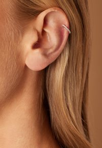 Silberne Creolen mit kleinen eingearbeiteten Edelsteinen; elegantes, abgerundetes Design passt eng um das obere Ohr. Braune Haare teilweise sichtbar.