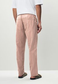 Lyserøde fløjlshorsebukser med hvide lodrette striber, med en afslappet pasform og elastisk talje, set bagfra.