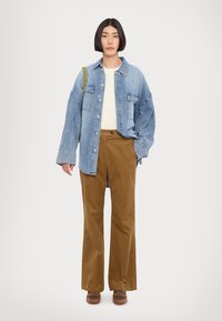 Denims oversize krekls, balts ribota džemperis, brūnas kordūras bikses, brūni apavi. Ikdienišķs apģērbs ar zaļu plecu siksnu uz krekla.