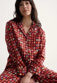 Piros mintás pizsama szett, amely zöld, sárga és rózsaszín gyémántformákat tartalmaz. Puha anyagból készült, gombos inggel és hosszú ujjakkal.