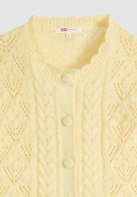 Weiche gelbe Strickjacke mit Zopfmustern, drei mit Stoff bezogenen Knöpfen und einem kleinen Levi's Markenlabel am Halsausschnitt.