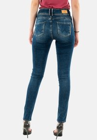 Jean skinny bleu à taille haute, avec deux poches arrière dotées de coutures courbées. Le matériau est du denim avec une légère élasticité.