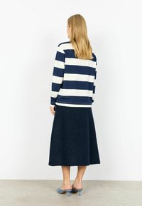 Tumesinise ja valge triibuline pika varrukaga ülaosa, mida on kombineeritud tumeda tekstuuriga seelikuga, viimistletud helesiniste sandaalide ning lihtsa tagumise vaatega.