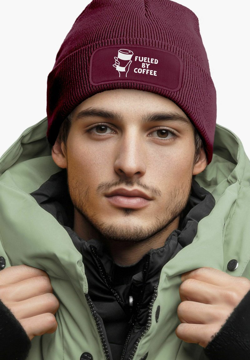 Maroon beanie with ribbed texture and white "FUELED BY COFFEE" graphic. Paired with a light green puffer jacket, featuring a black inner layer.