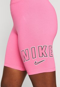 Rosa sportshorts gjorda av stretchigt tyg, med en stor svart "NIKE"-logotyp och en liten Nike swoosh-design på sidan.