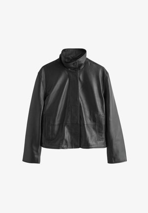 Mustast nahast jakk kõrge krae, ees nööbitav, kahe küljetasku ja siledat tekstuuri. Lõigatud keha järgivalt ja väheste õmblustega.