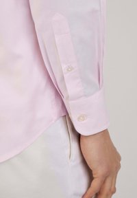 Camicia rosa chiaro a maniche lunghe con colletto strutturato e polsini abbottonati, con bottoni in perle e una texture in cotone liscio.