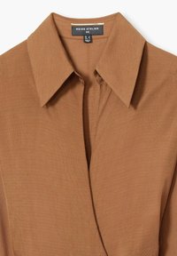 Bruin overhemd met kraag van gestructureerde stof met een voorpiek. Etiket leest "REISS ATELIER," maat 03, wat wijst op een op maat gemaakt ontwerp.