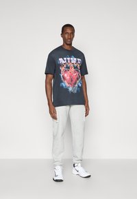 Μαύρο μπλούζα με πολύχρωμο γραφικό που απεικονίζει μια καρδιά και φλόγες. Συνδυασμένη με ανοιχτό γκρι φόρμα και λευκά αθλητικά παπούτσια. Απλός σχεδιασμός.