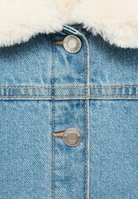 Jeans jakna z svetlo modrim pranjem, ki ima puhast bel ovratnik, srebrne zaponke na pritiskač in kontrastne oranžne šive.