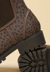 Bruine enkellaars met luipaardprint, elastisch paneel en patroon op de rubberen zool. Heeft een gestructureerd bovenwerk en versterkte stiksel-details.