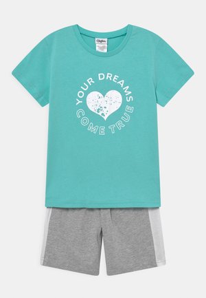 Türkises Baumwoll-T-Shirt mit einem Herz-Graphic und Text. Kombiniert mit grauen Shorts, die ein weißes Seitenpaneel haben.