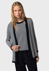 Randig stickad topp i marinblått och vitt, med långa ärmar och en enfärgad kant. Mjuk textur med en avslappnad passform. Kombineras med mörka byxor.