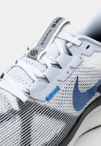 Nike løpesko med en hvit mesh-overdel og svarte og blå detaljer, runde lisser og et grått merke på tungen.