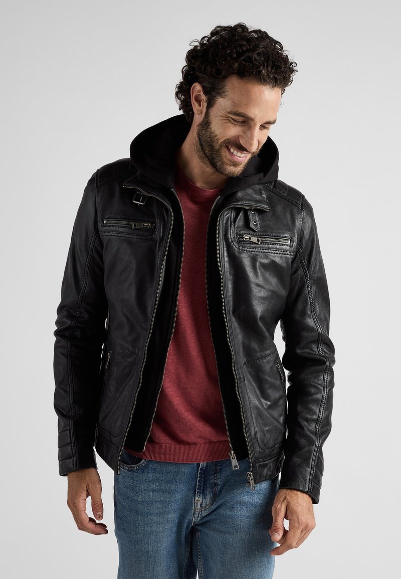 Zwarte leren jas met een afneembare capuchon, voorzien van ritszakken, een aansluitend ontwerp en ribbeltextuur op de mouwen. Draagt over een rood shirt.