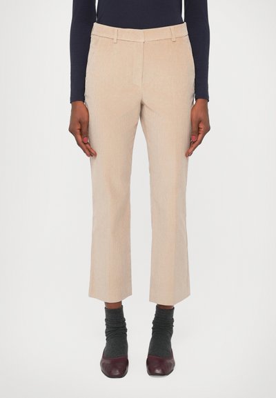 Beige Cordhosen mit geradem Schnitt, verkürzter Länge und seitlichen Taschen, kombiniert mit grauen Socken und bordeauxfarbenen Schuhen.