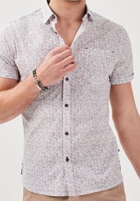 Short-sleeve shirt in light fabric with a zigzag pattern in white, navy, and red. Features a button-down collar and brown buttons.