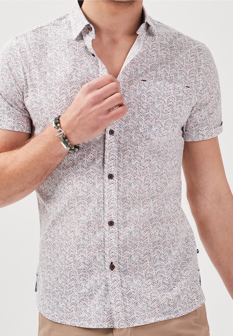 Short-sleeve shirt in light fabric with a zigzag pattern in white, navy, and red. Features a button-down collar and brown buttons.