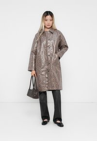 Leopard print, glossy, mid-length raincoat with front buttons, two side pockets, and a collar, worn over black trousers and flats.