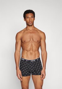 Schwarze Baumwollboxershorts mit wiederholt aufgedrucktem weißen Nike-Swoosh-Logo, die eine enganliegende Passform und einen elastischen Bund mit "NIKE"-Branding aufweisen.