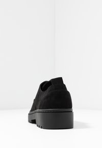 Chaussure en daim noir à talon bas, à bout arrondi et surface texturée. Présente des détails cousus et une languette à l'arrière.