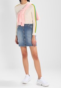 Ljust färgad stickad tröja med gröna och gula ränder, kombinerad med en denimbakknäppad kjol och vita sneakers, med en rosa topp draperad.