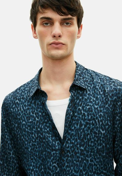 Donkerblauw shirt met luipaardprint, voorzien van een button-down kraag en contrasterende zwarte knopen, gelaagd over een wit onderhemd. Soepele stoftextuur.