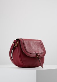 Borsa rotonda in pelle bordeaux con una finitura testurizzata, dotata di chiusura a patta, hardware dorato e tracolla.