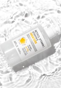 Flacon pompe en plastique transparent de gel douche corps au rétinol, vitamine C et E, étiqueté avec un contenu en rétinol de 4,7 %, flottant sur une surface d'eau ondulée.