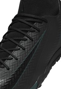 Black athletic shoe featuring a textured synthetic upper, flat black shoelaces, and a subtle green accent along the side. Rounded heel design.