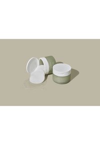 Twee ronde containers met witte deksels, één rechtop en één omgevallen, met heldere gel en ronde wattenpads in de buurt op een beige achtergrond.