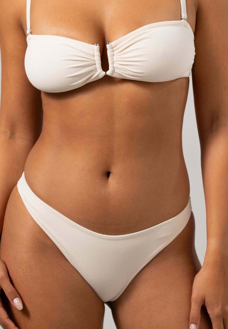 Vitt bikini-set som har en bandeau-topp med rynkning och framknäppning, tillsammans med lågriskade botten. Slät textur och minimalistisk design.