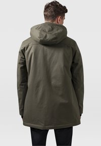 Olivnozeleni parka plašč s snemljivo kapuco, gladka tekstura in nekoliko podaljšan kroj. Ima preprost dizajn in minimalne akcenta.