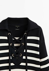 Pull rayé noir et blanc, en coton, avec un large col, un devant à lacets avec œillets en métal, et un tissu maille texturé.