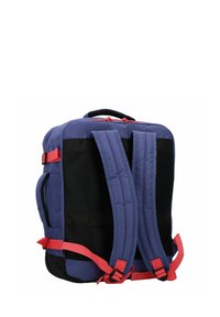 Zaino in tessuto blu con strap e dettagli rossi. Presenta un'imbottitura in rete sul retro, due tasche laterali e una maniglia superiore.