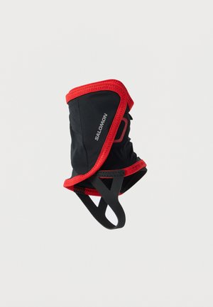 Polsino Salomon nero e rosso con cinturino elastico per il piede, progettato per la protezione della caviglia all'aperto e la prevenzione dei detriti.