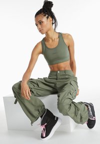 Olive green sports bra and cargo pants with multiple pockets, paired with black high-top sneakers featuring pink laces and leopard print lining.