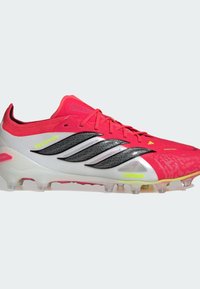 Chaussures de football roses avec une tige texturée, des accents argentés et des bandes noires. Elles disposent de crampons transparents pour l'adhérence et d'un design épuré.