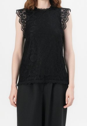 Top in pizzo nero con bordi ondulati e motivi floreali intricati, privo di maniche e con un collo alto. Abbinato a pantaloni neri.