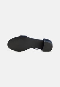 Sinine sametist kõrge kontsaga sandaal suletud tagumise osa ja avatud toe ning tekstuuriga musta tallaga, millel on minimalistlik rihmade disain.