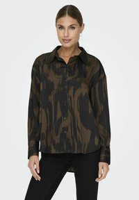 Camicia a maniche lunghe marrone e nera con motivo, con apertura frontale a bottoni e colletto, caratterizzata da un taglio rilassato e un orlo leggermente curvo.