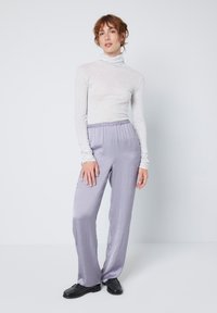 Světle šedý dlouhý rolák s přiléhavým střihem, doplněný o volné kalhoty levandulové barvy z jemné, hladké látky. Černé boty dokončují outfit.