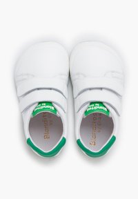Zapatos de cuero blanco con dos correas de Velcro y acentos verdes en el talón. Textura suave, punta redondeada y marca dorada en relieve en el interior.