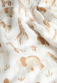 Cotton fabric features a whimsical animal print in soft beige and brown hues, showcasing elephants, giraffes, and leafy accents on a white background.