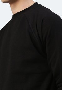 Felpa nera a maniche lunghe con collo a girocollo e maniche raglan, caratterizzata da una texture liscia e dettagli di cucitura minimi.