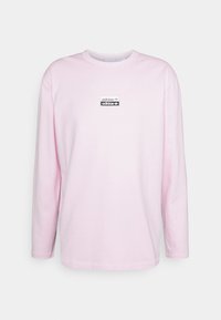 Ljusrosa långärmad t-shirt i bomull. Har en svart rektangulär adidas-logopatch på bröstet. Rund halsringning och rak nederkant.