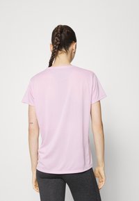 Camiseta rosa clara de manga corta con escote redondo, textura suave y corte relajado, combinada con leggings gris oscuro. Vista trasera.
